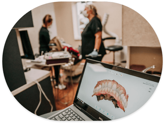 Model of teeth on computer monitor with dental patient being treated in background