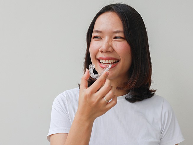 Woman smiling while holding clear aligner
