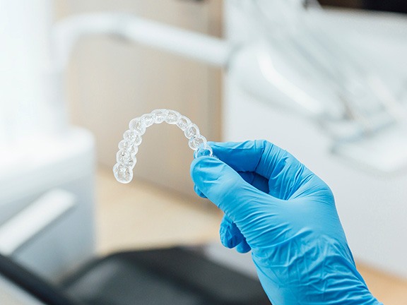 Dentist with blue gloves holding clear aligner