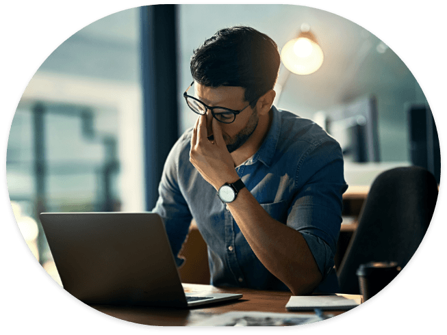 Man at desk with laptop pinching the bridge of his nose